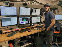 Elias Adediran stands before an array of monitors showing data acquisition from the ship's sensors.