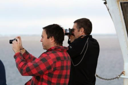 Roland Arsenault and John Farrel on the deck of the Healy taking photographs of a polar bear.