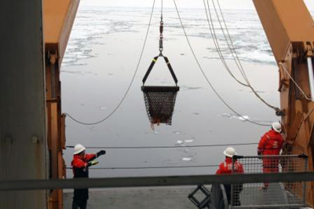 Suspended dredge bucket is guided aboard Healy over the stern. 